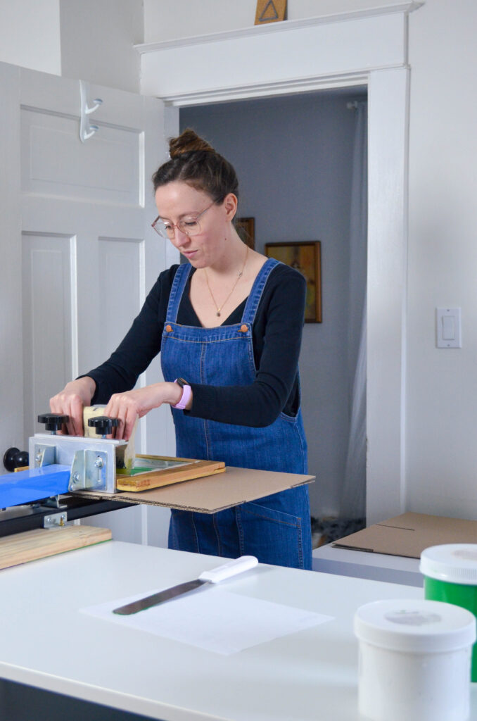 A woman wearing a denim jumper screen prints a logo on a box.