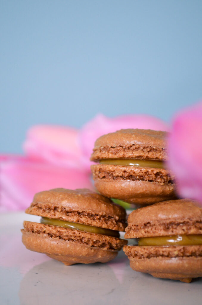 Chocolate macarons filled with dulce de leche, surrounded by pink tulips.