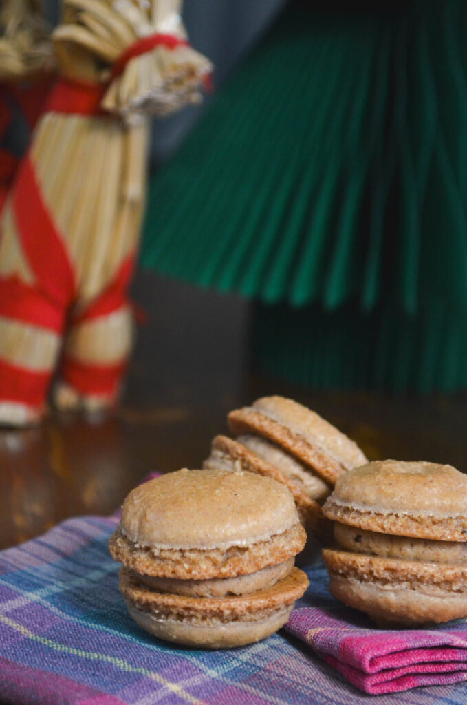 Three gingerbread macarons with small yule goat and paper tree decoration.